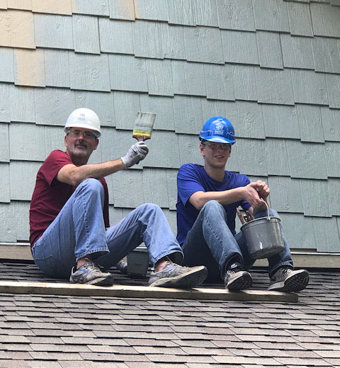 Windsor employees help repaint a homes exteriors on the roof